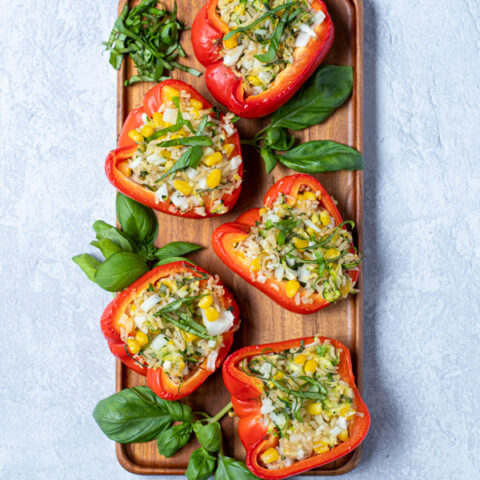 flatly of stuffed red bell peppers arranged on a wooden tray next to fresh basil leaves