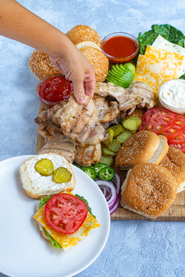 hand grabbing a chicken thigh off of the platter to put on a sandwich