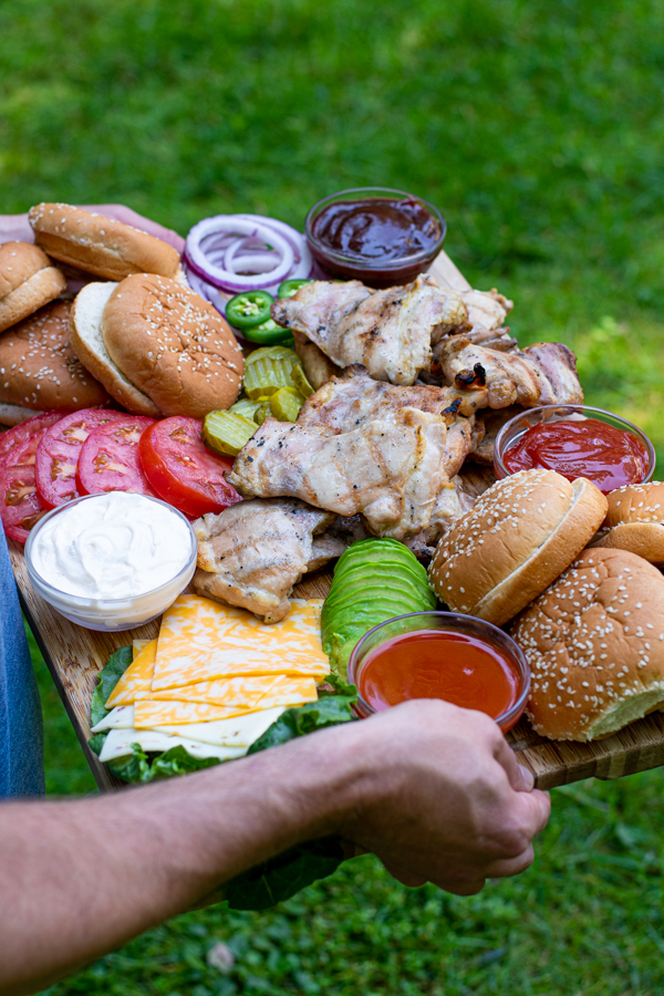 over shoulder shot of a man carrying a large board filled with grilled chicken, buns, and toppings