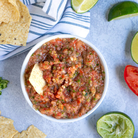 overhead view of fresh salsa made in the food processor in a white bowl surrounded by tortilla chips and lime wedges