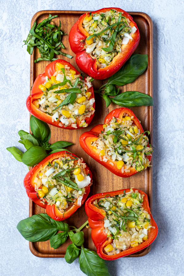 overhead view of a wooden platter of stuffed red bell peppers arranged next to basil leaves