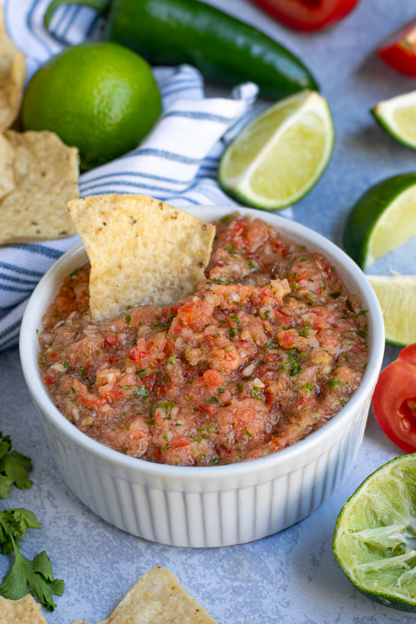 white bowl of freshly made salsa using fresh tomatoes with a tortilla chip sticking out