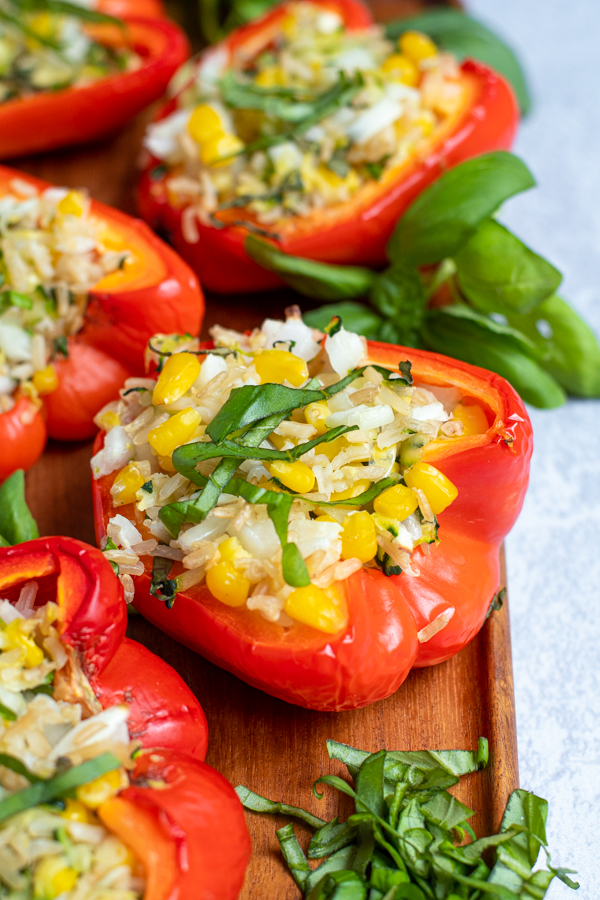 close up of a vegetarian grilled stuffed red bell pepper on a wooden board next to basil leaves