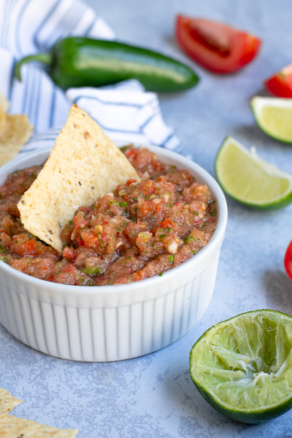 close up of freshly made salsa in a white bowl with a tortilla chip sticking out