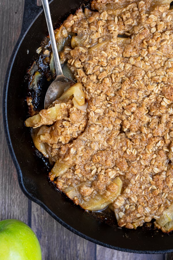 serving spoon in apple crisp in a cast iron skillet showing apples covered in the crisp oat topping