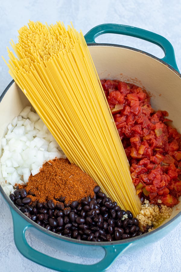 all the uncooked ingredients for taco spaghetti in a teal dutch oven pot