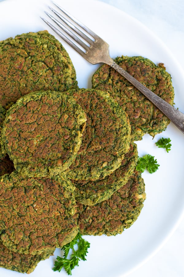 oven baked falafel piled on a white plate next to parsley and a fork