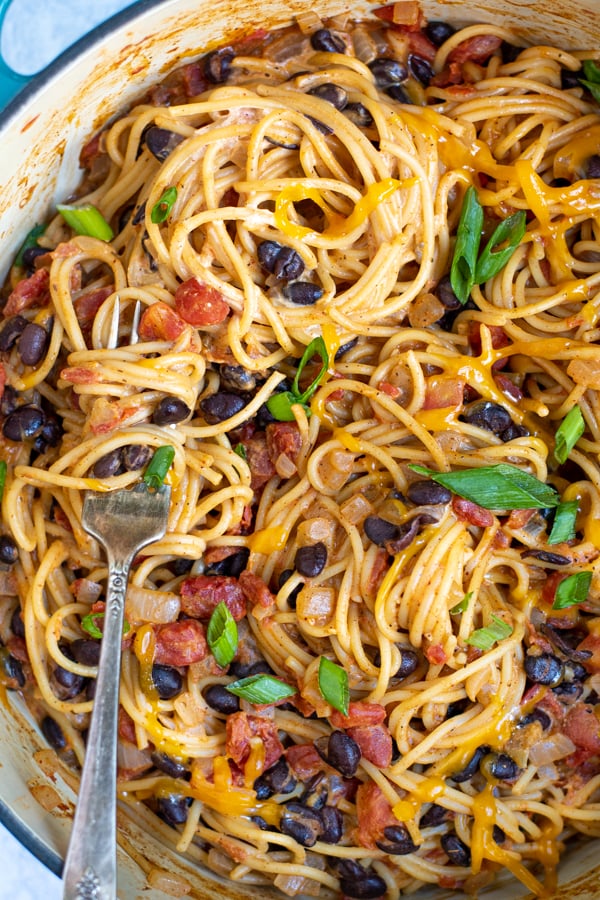 close up of taco spaghetti with black beans, tomatoes, cheese, and green onions