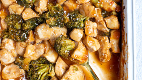 serving spoon in a saucy baking dish full of general tso chicken a broccoli