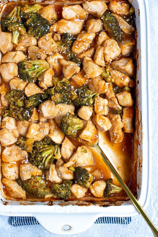 serving spoon in a saucy baking dish full of general tso chicken a broccoli