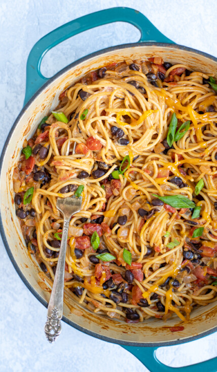 one pot taco spaghetti made from black beans and pasta in a large teal pot with a fork swirled with the pasta