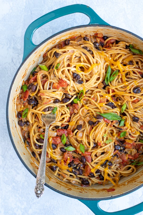 one pot taco spaghetti made from black beans and pasta in a large teal pot with a fork swirled with the pasta