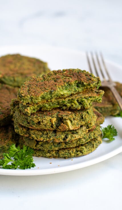Stack of healthy oven baked falafel on a plate with the top falafel broken open to reveal a green inside