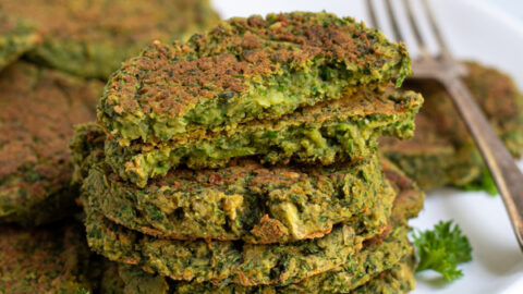 Stack of healthy oven baked falafel on a plate with the top falafel broken open to reveal a green inside