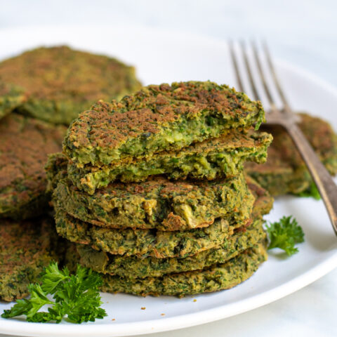 Stack of healthy oven baked falafel on a plate with the top falafel broken open to reveal a green inside