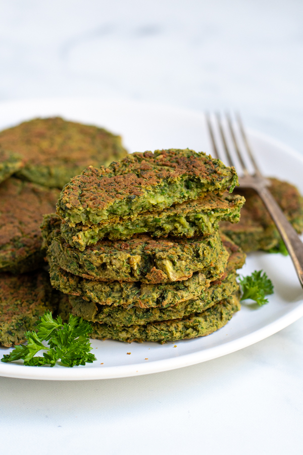 Stack of healthy oven baked falafel on a plate with the top falafel broken open to reveal a green inside