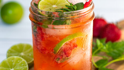 drinking glass jar filled with a bright pink Strawberry Mojito Mocktail made with lime seltzer and garnished with lime slices and fresh mint leaves