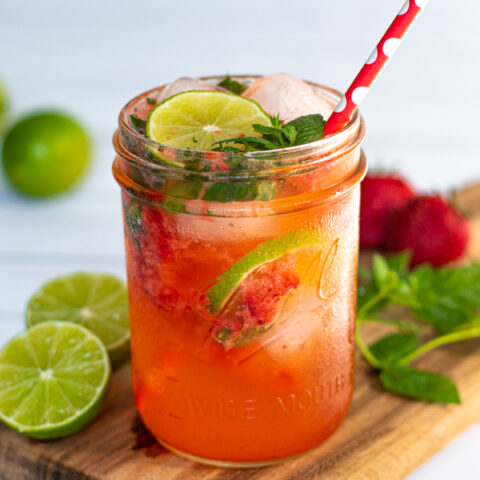 drinking glass jar filled with a bright pink Strawberry Mojito Mocktail made with lime seltzer and garnished with lime slices and fresh mint leaves