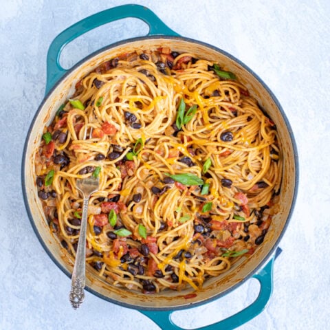 vegetarian taco spaghetti in a large teal dutch oven pot garnished with shredded cheese and green onions