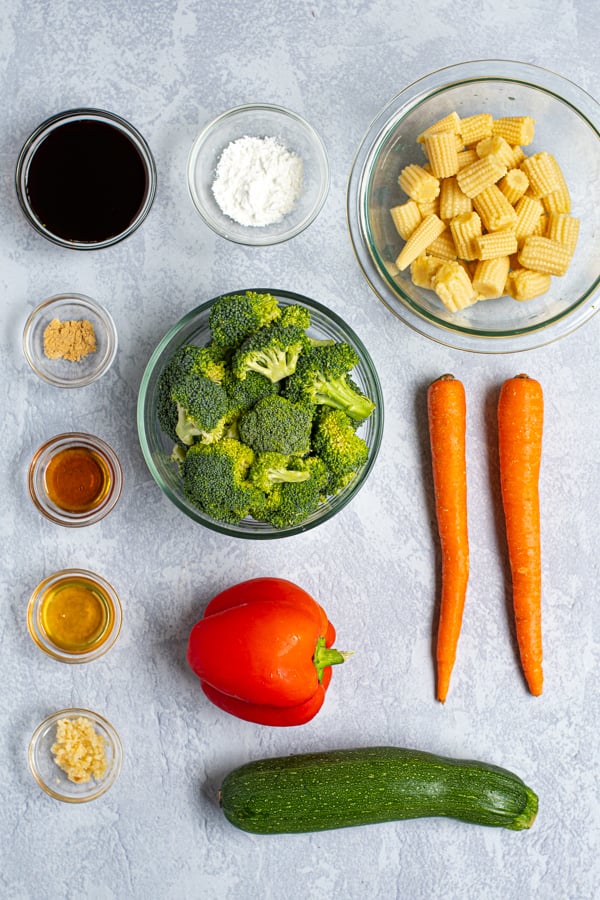 ingredients needed to make an easy vegetable stir fry laying on a table top including veggies and ingredients for the sauce