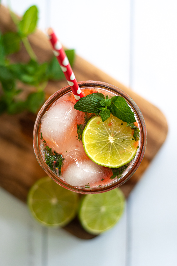 an overhead view of a glass of strawberry mojito mocktail showing lime slices and fresh mint as garnishes
