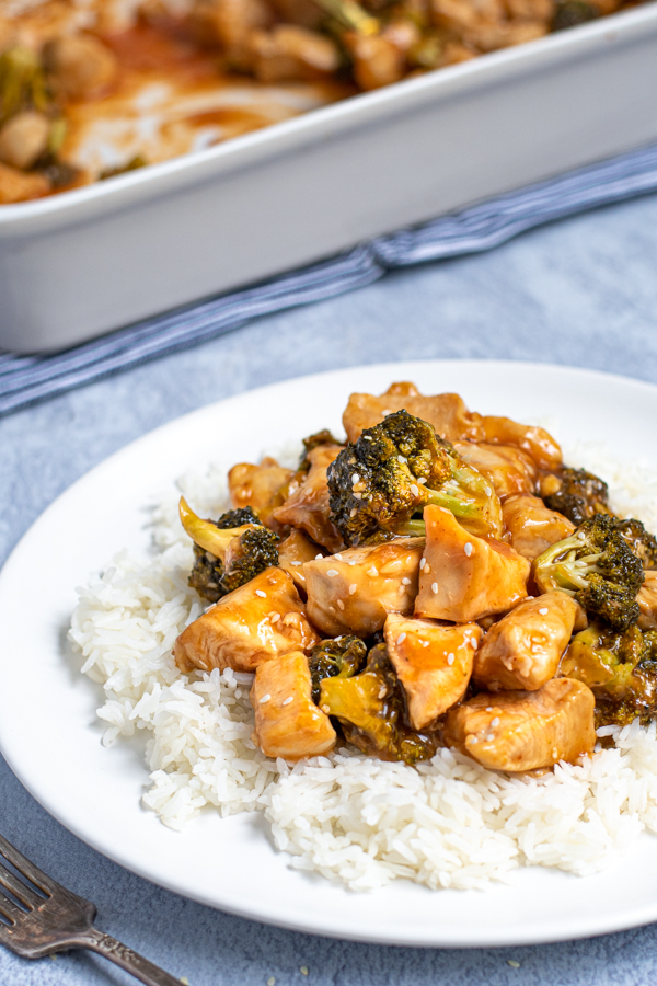 a large scoop of baked general tso chicken on a bed of rice on a white plate with broccoli