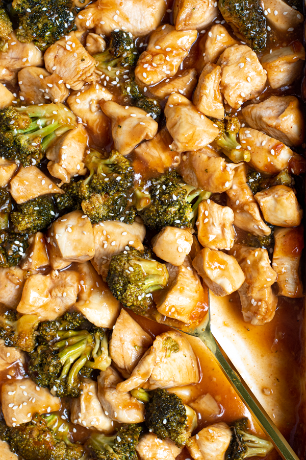 a large gold serving spoon in a baking dish filled with saucy general tso chicken