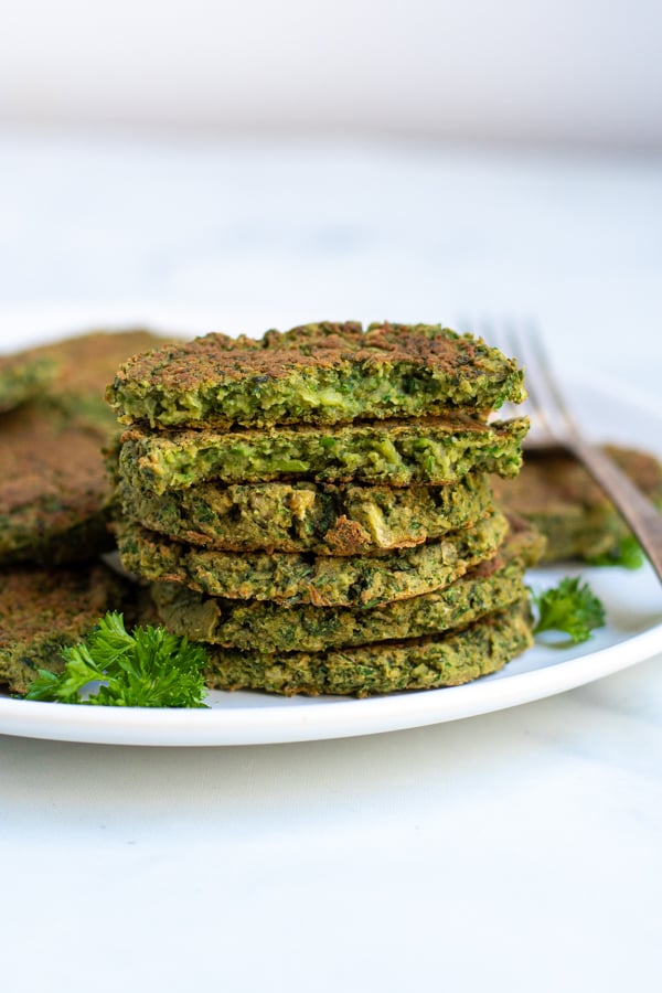 a stack of baked falafel on a white plate with the top patty broken open to reveal inside