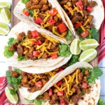 Pinterest Pin with text overlay Easy Chicken Tacos showing photo of chicken tacos in flour tortillas on a board with cheese, tomatoes, and lime wedges.