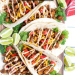 Pinterest Pin with text overlay Quick and Easy Chicken Tacos showing a platter of chicken tacos in flour tortillas next to a red towel and slices of limes.
