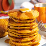 Pinterest Pin with Text overlay Pumpkin Spice Pancakes with image of a stack of pancakes on a white plate topped with a rad of butter and maple syrup dripping down the sides of the pancakes.