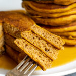 Pinterest Pin with Text overlay Pumpkin Spice Pancakes image shows a fork with a stack of three pieces of cut pancake relieving a fluffy interior.