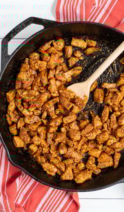 Easy Chicken Tacos being made in a cast iron pan, saucy chicken pieces covered in seasoning.