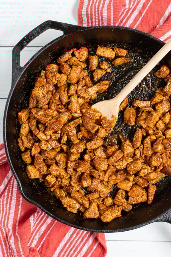 Easy Chicken Tacos being made in a cast iron pan, saucy chicken pieces covered in seasoning.