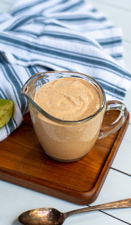 Serving glass with handle filled to the top with healthy southwest sauce sitting next to a kitchen towel and spoon.