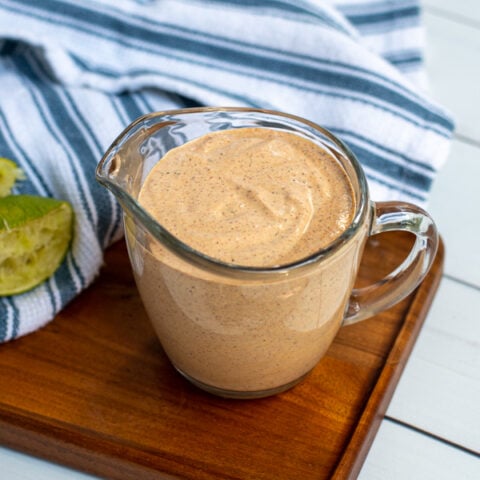 Serving glass with handle filled to the top with healthy southwest sauce sitting next to a kitchen towel and spoon.