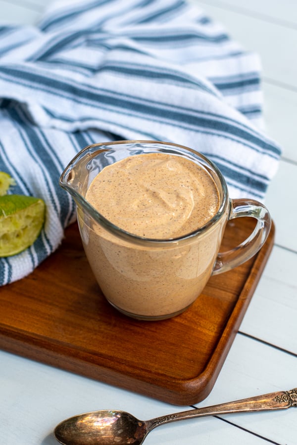 Serving glass with handle filled to the top with healthy southwest sauce sitting next to a kitchen towel and spoon.