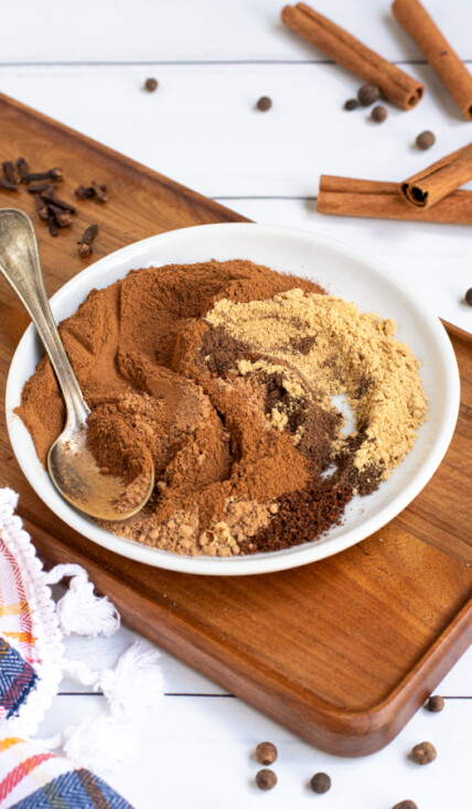 a small white plate on a cutting board filled with mixed together spices of varying shades of browns, once fully blended will be pumpkin pie spice.