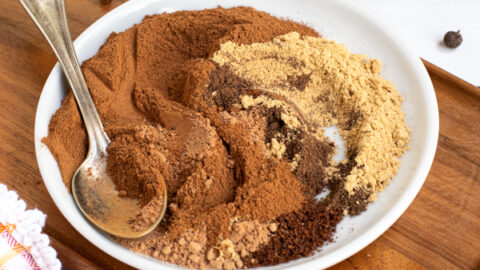 a small white plate on a cutting board filled with mixed together spices of varying shades of browns, once fully blended will be pumpkin pie spice.