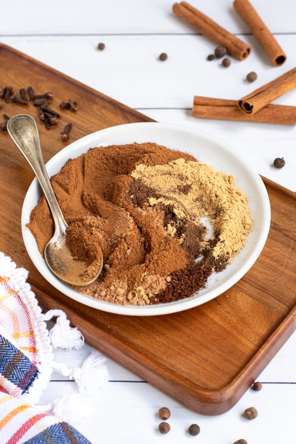 a small white plate on a cutting board filled with mixed together spices of varying shades of browns, once fully blended will be pumpkin pie spice.