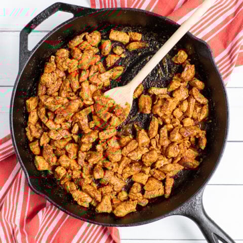 Easy chicken taco filling in a cart iron pan with a wooden spoon scooping the filling.