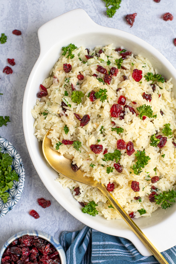 Overhead view of a serving dish full of white rice with onions, dried cranberries, and parsley to garnish.