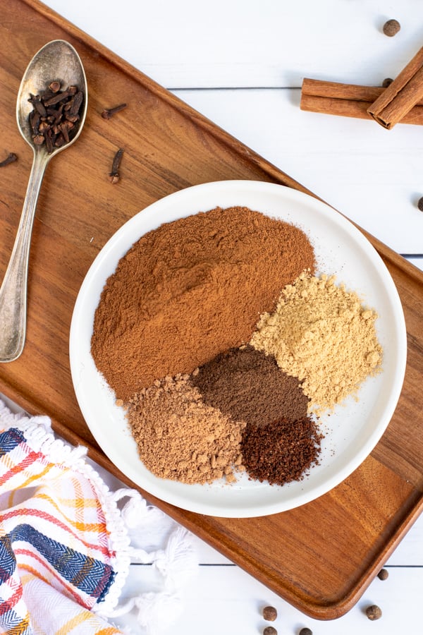 overhead photo of a small white plate on a wood cutting board, on the plate is 5 spice piles used to make pumpkin spice blend.