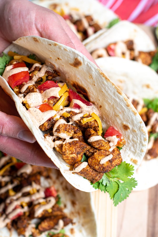 hand holding a taco over a plate filled with chicken, tomatoes, cheese, and sauces.