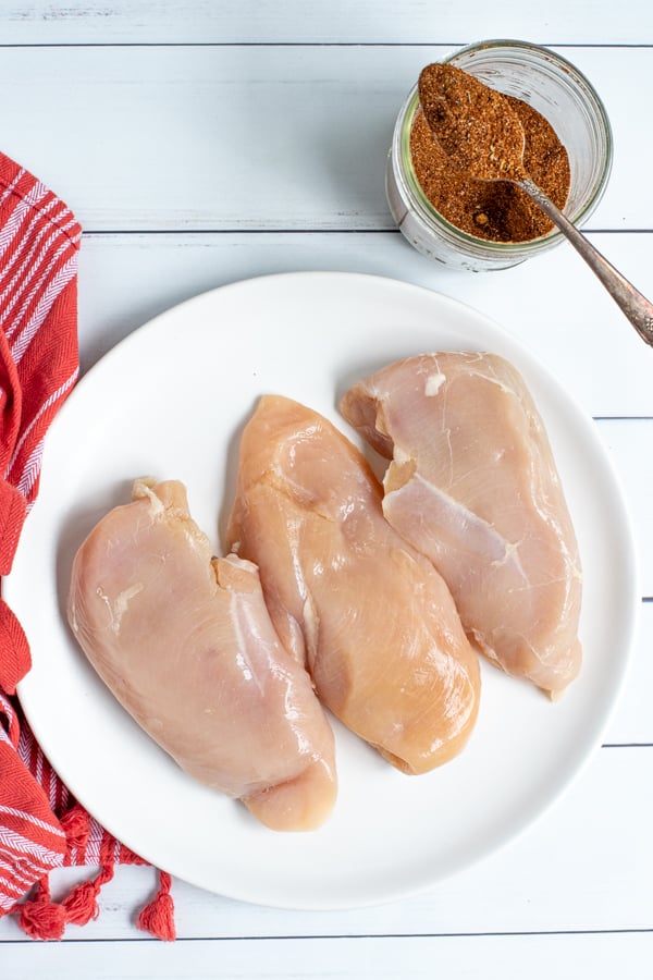 Ingredients on a table for easy chicken tacos, chicken breasts and a jar of taco seasoning.