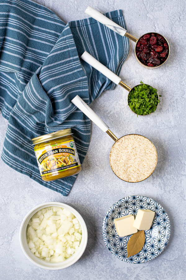 Ingredients needed for cranberry rice pilaf laid out on a table with a kitchen towel.