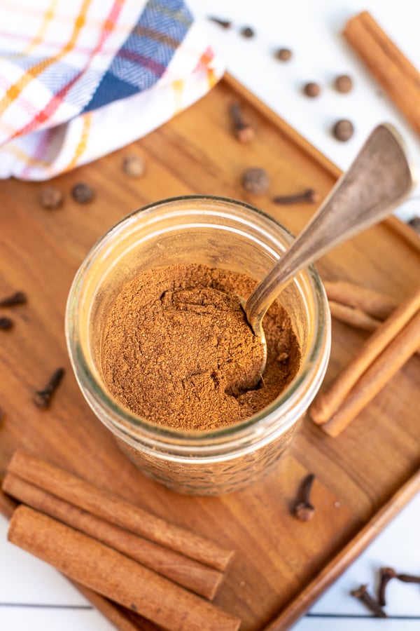 A small jar on a wooden board, in the jar is a spoon and a brown pumpkin pie spice blend.