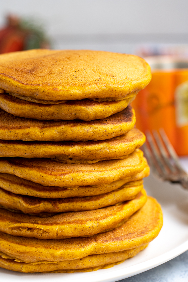 Close view of a high stack of pumpkin pancakes on a white plate next to a fork.