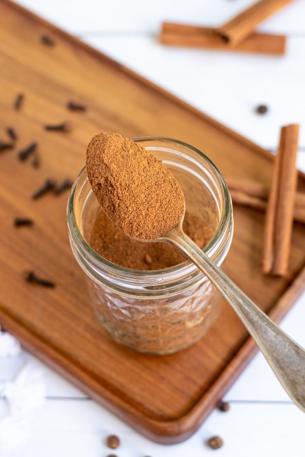 Spoon resting on the edge of a jar with a scoop of brown pumpkin pie spice mixture.