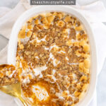 Pinterest Pin with Text: Sweet Potato Casserole with Marshmallow & Oat Streusel, showing a casserole in a white baking dish with a gold serving spoon with a scoop out of it.